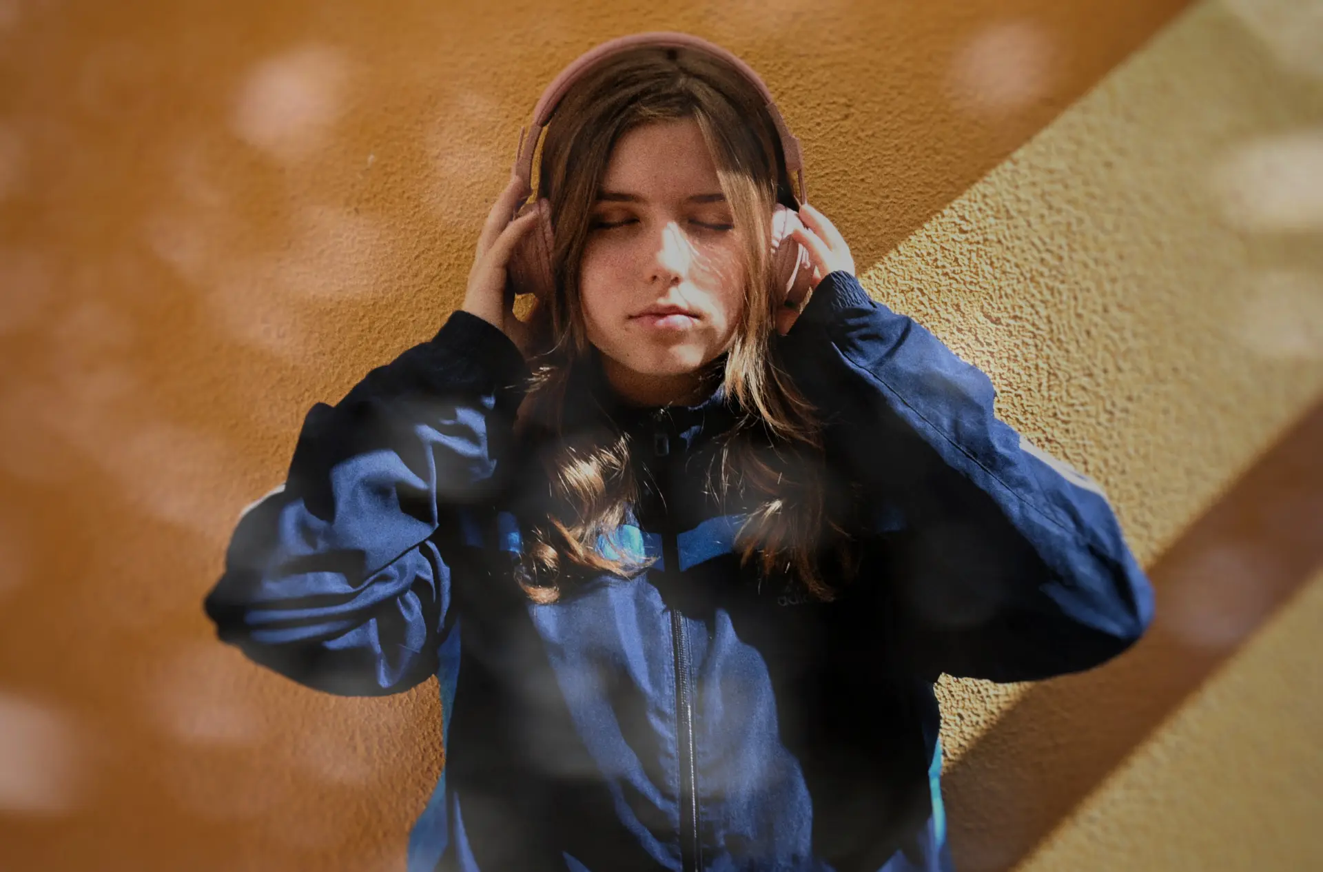 Noia adolescent recolzada en una paret, amb auriculars posats, en un moment de calma sensorial